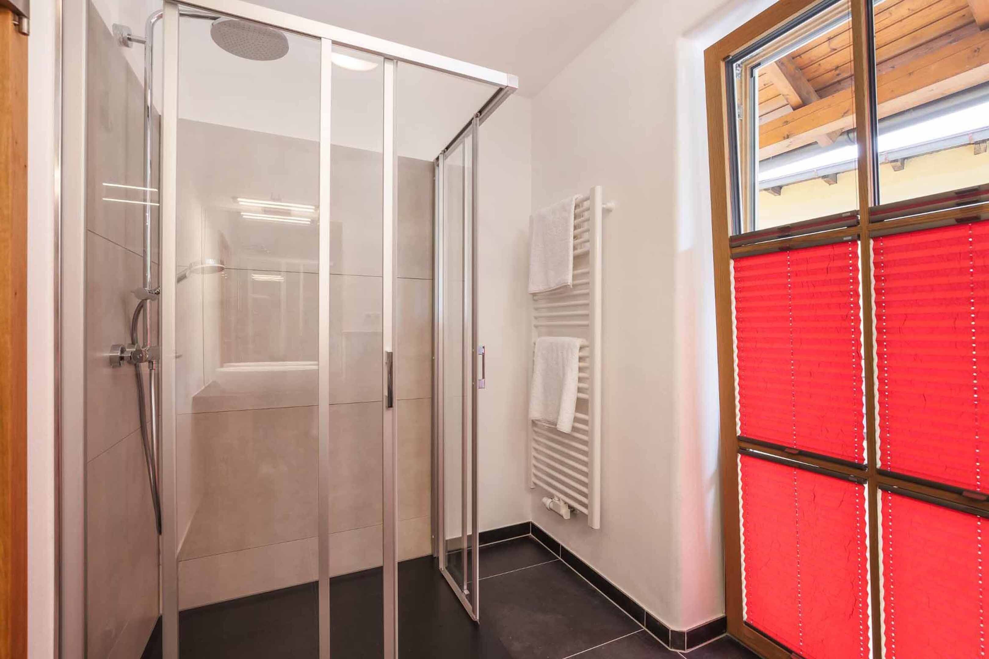 Un baño moderno con cabina de ducha de vidrio, un perchero blanco y una persiana roja.