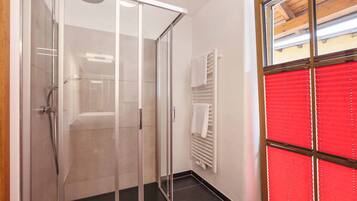 Un baño moderno con cabina de ducha de vidrio, un perchero blanco y una persiana roja.