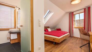 A bedroom with a wooden bed, a red blanket, a chair, and a window with curtains.