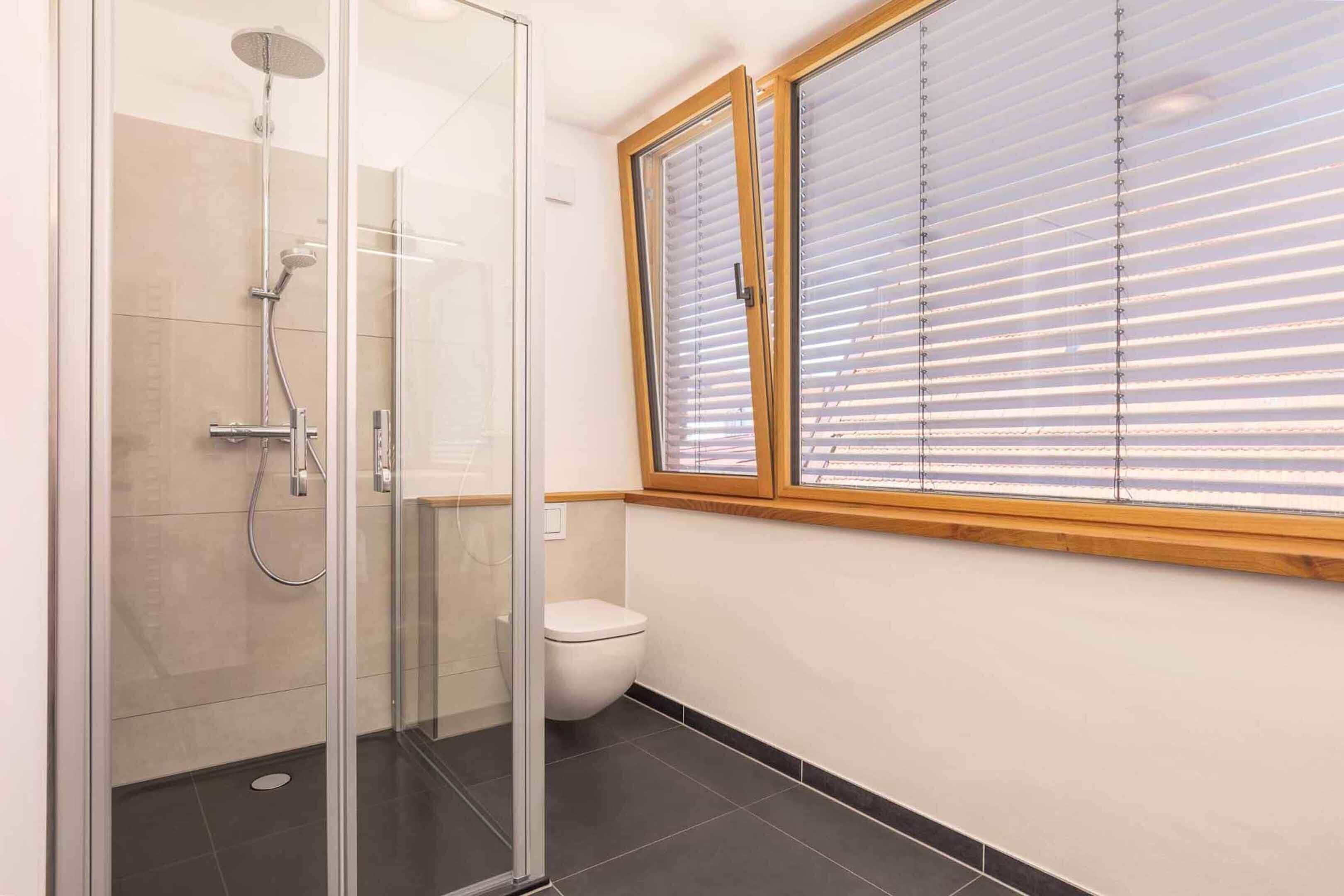 Ein Badezimmer mit einer einteiligen Duschkabine, Toilette und einem Fenster mit Jalousien.