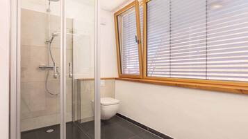 Ein Badezimmer mit einer einteiligen Duschkabine, Toilette und einem Fenster mit Jalousien.