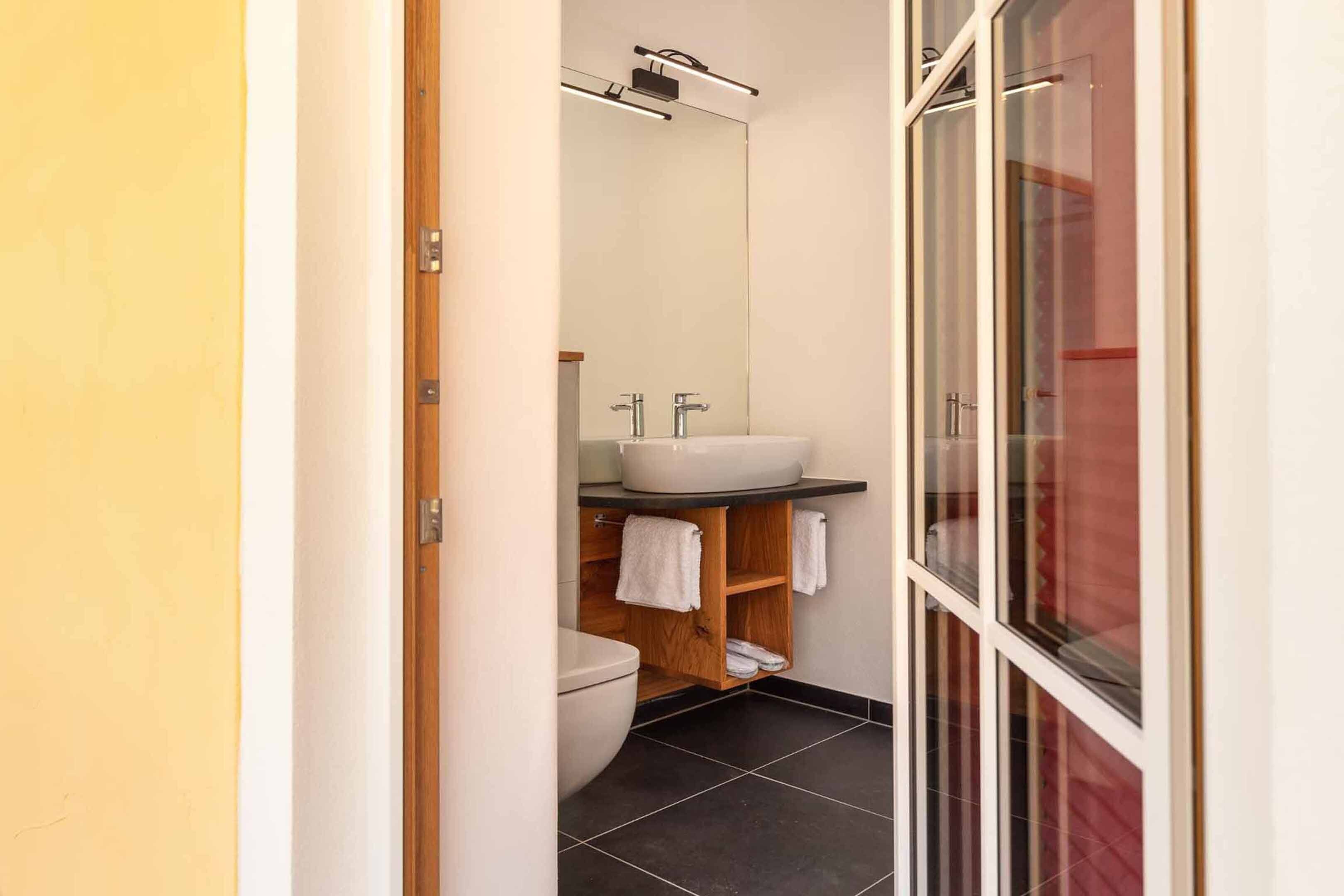 Un baño moderno con un lavamanos blanco, dos toalleros, un armario de madera y una cabina de ducha de vidrio.