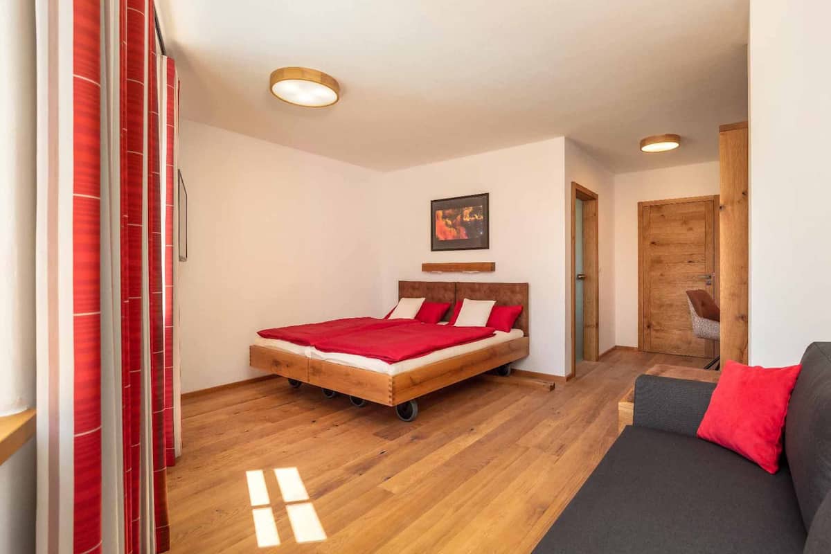 Une chambre avec un lit en bois, un canapé gris et une couverture rouge.