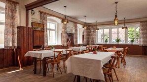 Un espace repas avec des tables et des chaises en bois, de grandes fenêtres avec des rideaux et des lampes suspendues.