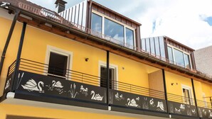 Un immeuble à plusieurs étages, doté d’une façade jaune, d’un balcon orné de motifs représentant des cygnes et des plantes aquatiques, et de grandes fenêtres.