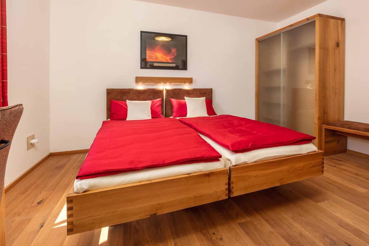 Une chambre à coucher moderne avec un lit en bois, une literie rouge, une œuvre d’art accrochée au mur et une armoire en bois.