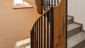 Un escalier en colimaçon avec des marches en bois et des rampes noires, menant à l’étage supérieur.