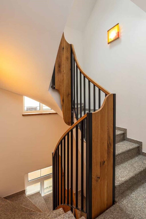 Un escalier en colimaçon avec des marches en bois et des rampes noires, menant à l’étage supérieur.