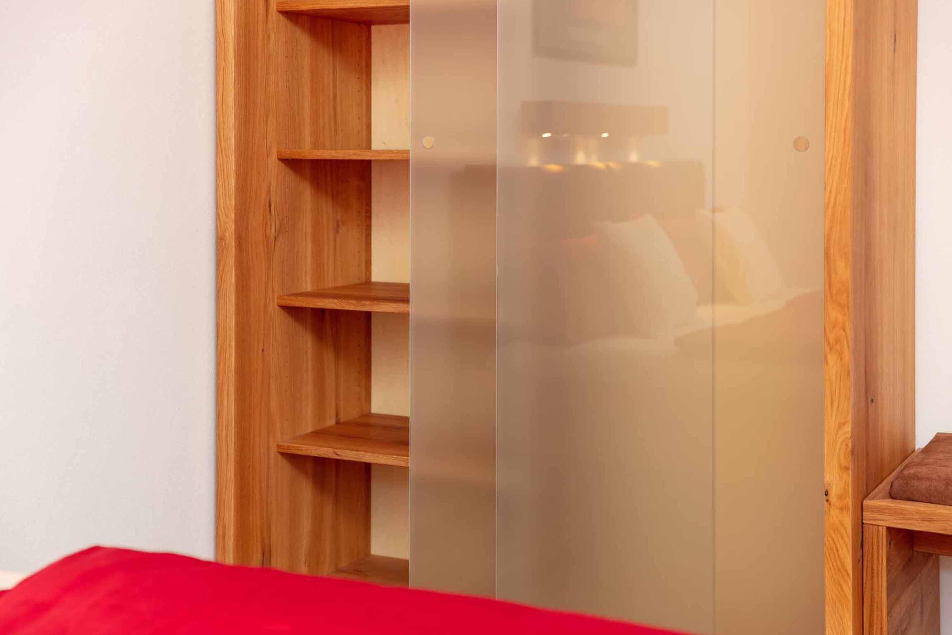 A wooden wardrobe with multiple shelves and a mirrored door.