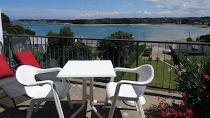 A balcony with a table and chairs, overlooking a beach and sea.