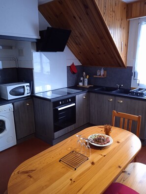 A compact kitchen with modern appliances, a wooden dining table, and a view of the outdoors.