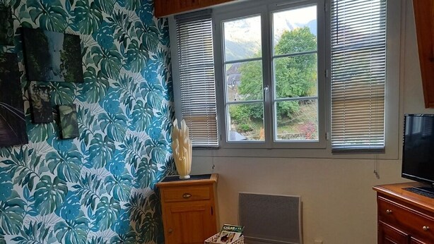 Un salon doté d’un plancher en bois, d’un canapé bleu, d’une table ronde avec un panier, et d’une grande fenêtre avec des stores.