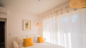 Une chambre à coucher avec un lit, deux oreillers jaunes, un tableau encadré au mur et une fenêtre avec des rideaux.