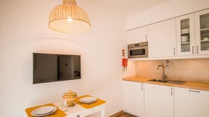 Une cuisine compacte avec des meubles blancs, un four à micro-ondes, un évier et une table à manger, le tout agrémenté d’assiettes et d’un saladier.