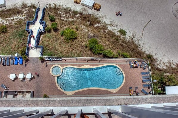 A swimming pool with a wavy edge, surrounded by lounge chairs and a small hot tub.