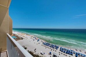 A beach with umbrellas and lounge chairs, a pool, and a view of the ocean.