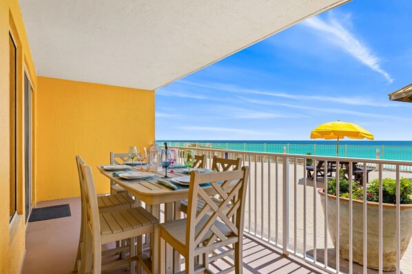 A balcony with a table set for dining, a yellow umbrella, and a view of the beach.