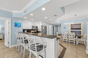 A modern kitchen with white cabinetry, a granite countertop, and a dining area with white chairs.