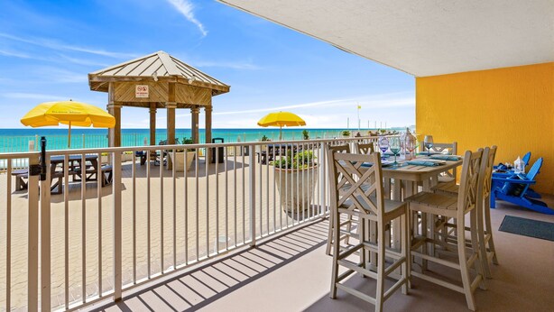 Ein Balkon mit Blick auf den Strand, ein hölzernes Pavillon und gelbe Sonnenschirme.
