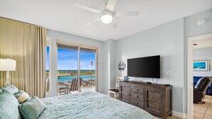 A bedroom with a bed, a TV, a dresser, and a view of a pool and beach. - Oceanfront escape - pool, hot tub & attraction tickets (Panama City Beach)