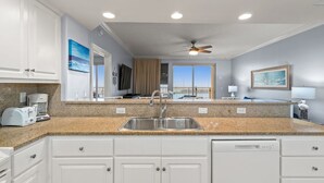 A modern kitchen with white cabinets, a granite countertop, a double sink, and a ceiling fan. - Oceanfront escape - pool, hot tub & attraction tickets (Panama City Beach)