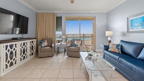 A living room with a TV, two armchairs, a sofa, a coffee table, and a balcony with a view. - Oceanfront escape - pool, hot tub & attraction tickets (Panama City Beach)