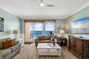 Un salon comprenant un canapé, une table basse et un téléviseur. Il y a un balcon avec vue sur l’océan.