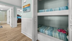 Quarto com beliches, porta dando acesso a outro cômodo, um quadro na parede e piso de madeira.