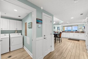 A laundry room with two washing machines, a dining area with a table and chairs, and a kitchen with white cabinets and a window. - Gulf-view balcony w/ free attraction tickets (Panama City Beach)