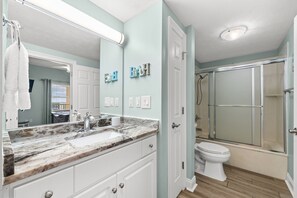 Ein Badezimmer mit Marmorwaschbecken, Toilette, Duschkabine mit Glastüren und einem Spiegel mit aufgehängtem Handtuch.