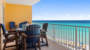 Een balkon met uitzicht op de oceaan, houten stoelen, een tafel met een glas en een witte lantaarn.