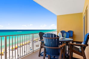 Un balcon avec vue sur la plage, des chaises bleues et une table avec un verre et une assiette.