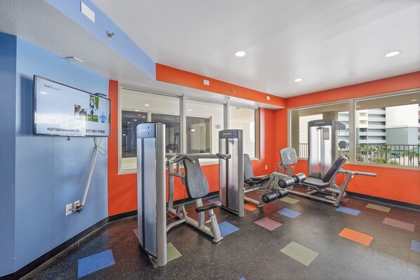 A gym with exercise equipment, a TV screen, and a window with a view of buildings.