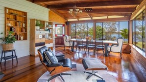 A spacious living area with a wooden ceiling, large windows, a dining table, and modern furniture. - Riverside Ranch - Oceanstays (Yamba)