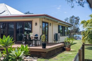 A house with a covered patio, a dining area with chairs and a table, and a large window. - Riverside Ranch - Oceanstays (Yamba)