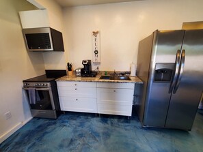 A kitchen with a stainless steel refrigerator, a built-in oven, and a microwave. There is a 'WELCOME' sign on the wall.