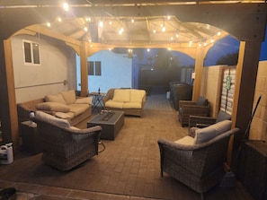 An outdoor patio area with wicker furniture, a fire pit, and string lights.