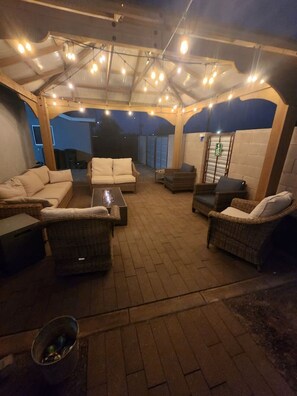 An outdoor patio area with a covered seating arrangement, including sofas and wicker chairs, under a canopy with string lights. - Downstairs studio on 13 st (Phoenix)