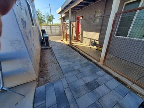 A paved pathway leading to a building with a red door and a fenced area.