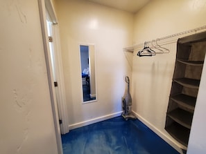 A narrow hallway with a blue floor, a mirror, a vacuum cleaner, and a shelving unit with hangers. - Downstairs studio on 13 st (Phoenix)