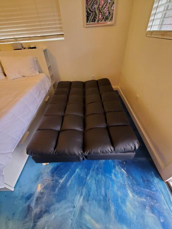 A small, single-bed room with a dark mattress and white bedding.
