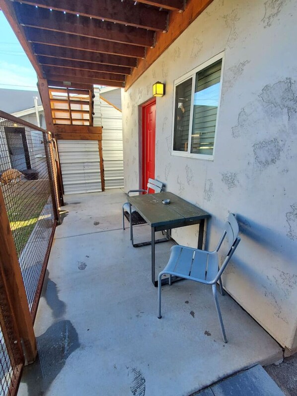 A covered patio area with a table and chairs, a red door, and a window.