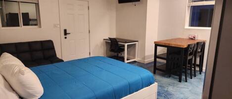 A bedroom with a bed, a desk, a chair, a TV, and a door.