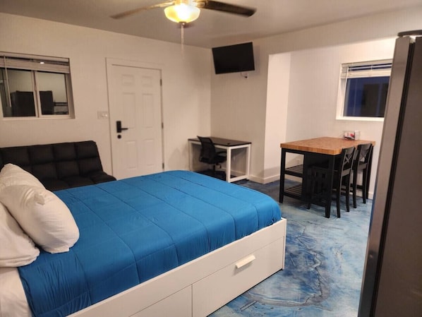A bedroom with a bed, a desk, a chair, a TV, and a door.