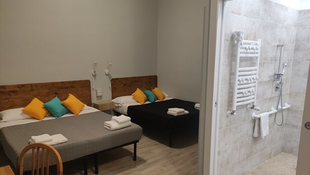 A hotel room with two beds, a wooden chair, a desk, and a shower area with a towel rack. - Hotel Big Bang (Rome)