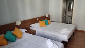 A hotel room with two beds, each with white linens and colorful pillows, a wooden headboard, a bedside lamp, and a bathroom visible through an open door. - Hotel Big Bang (Rome)