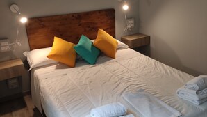 A neatly made bed with white linens and multiple pillows in various colors, two bedside lamps, and a wooden headboard. - Hotel Big Bang (Rome)