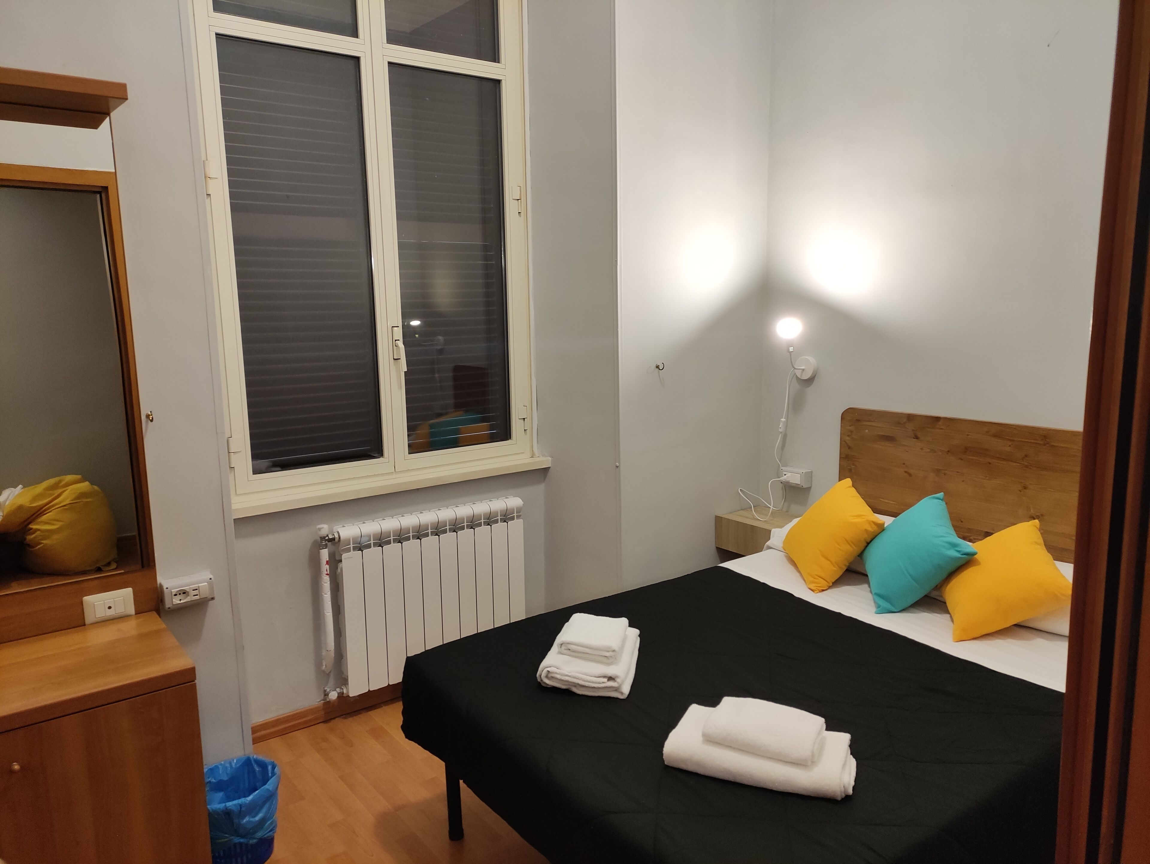 Une chambre à coucher bien rangée, avec un lit, une lampe de chevet et une fenêtre équipée de stores.