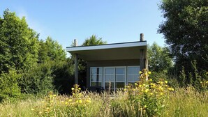 Een modern, gelijkvloers gebouw met grote ramen, omgeven door hoog gras en bloemen.