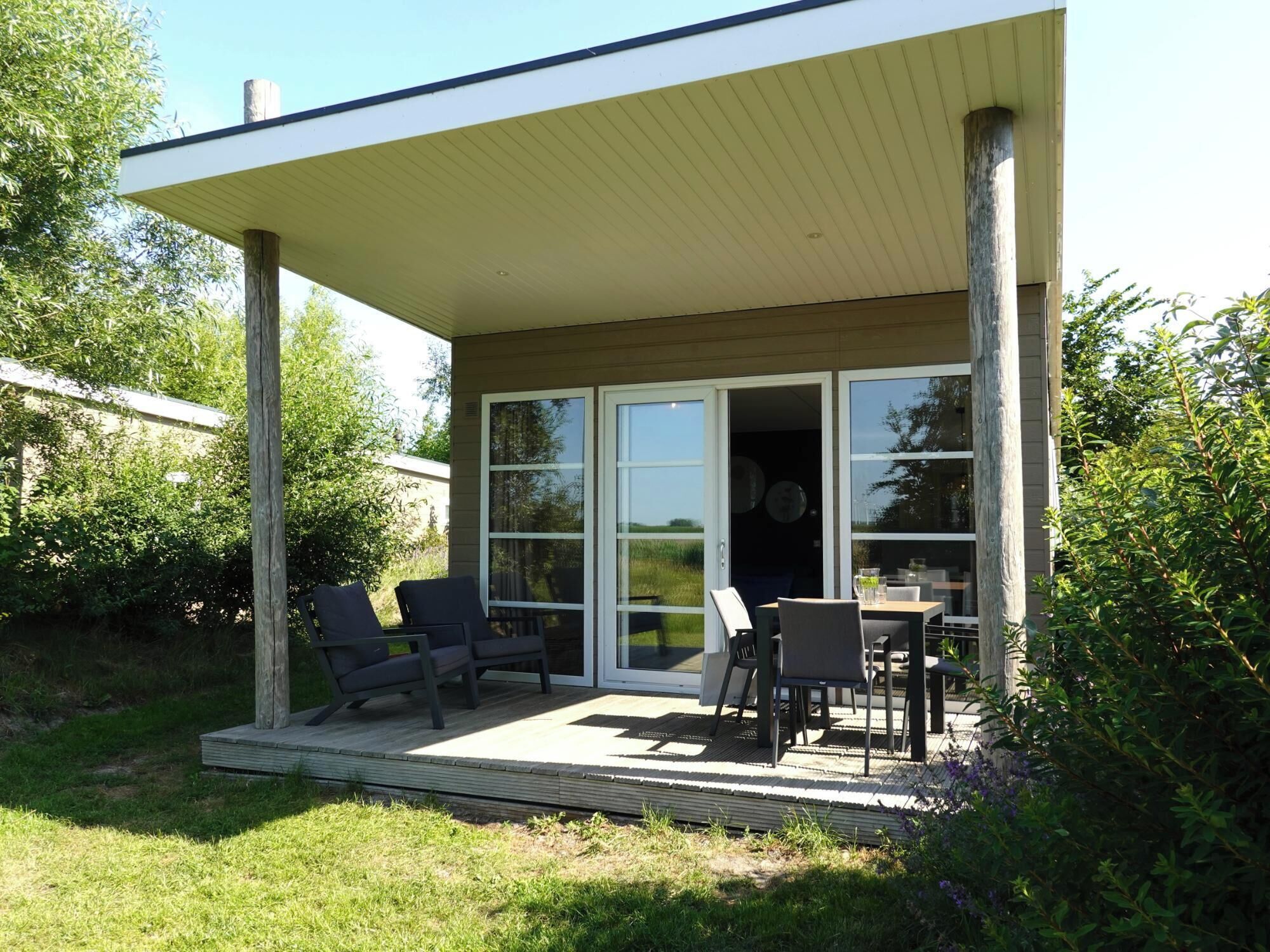 Eine überdachte Terrasse im Freien mit Tisch und Stühlen, umgeben von Grünpflanzen.